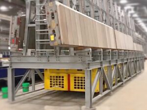 Gelbes und schwarzes mechanisches Maultier für den Transport von vorgefertigten Betonplatten in einer Industrieanlage, getragen von einer grauen Metallstruktur